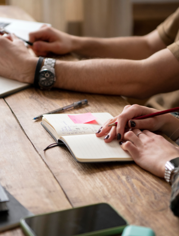 Duas pessoas a trabalharem numa secretária enquanto uma aponta notas num caderno